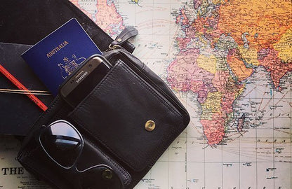 Black leather hip bag with sunglasses, passport, and phone on a world map
