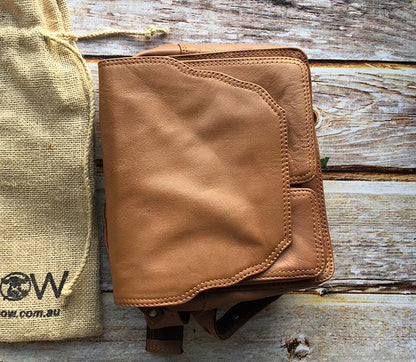 Brown leather pouch on a wooden surface with a beige fabric bag in the background.